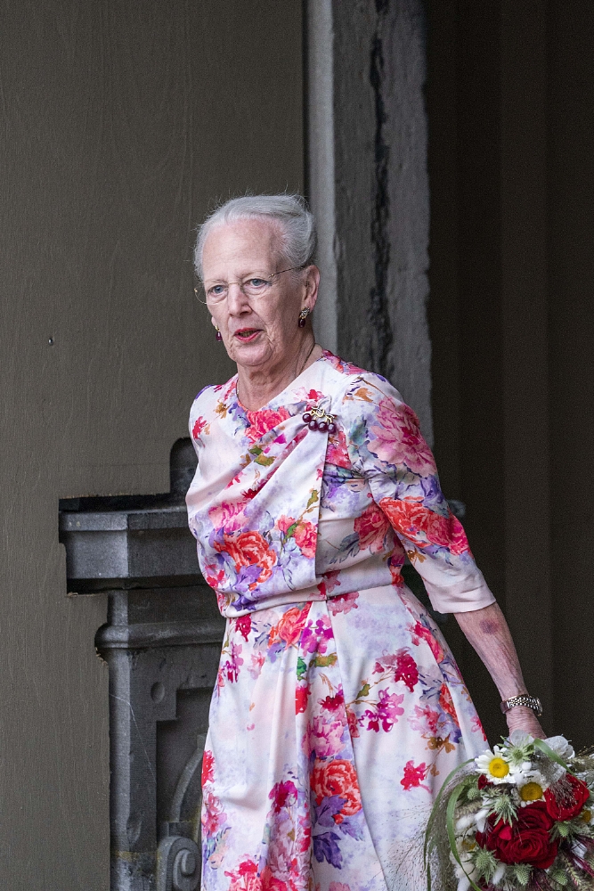 Queen Margrethe of Denmark wearing floral dress and holding flowers.
