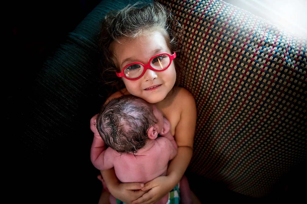 Heartwarming photo of little girl holding newborn brother she helped deliver goes viral
