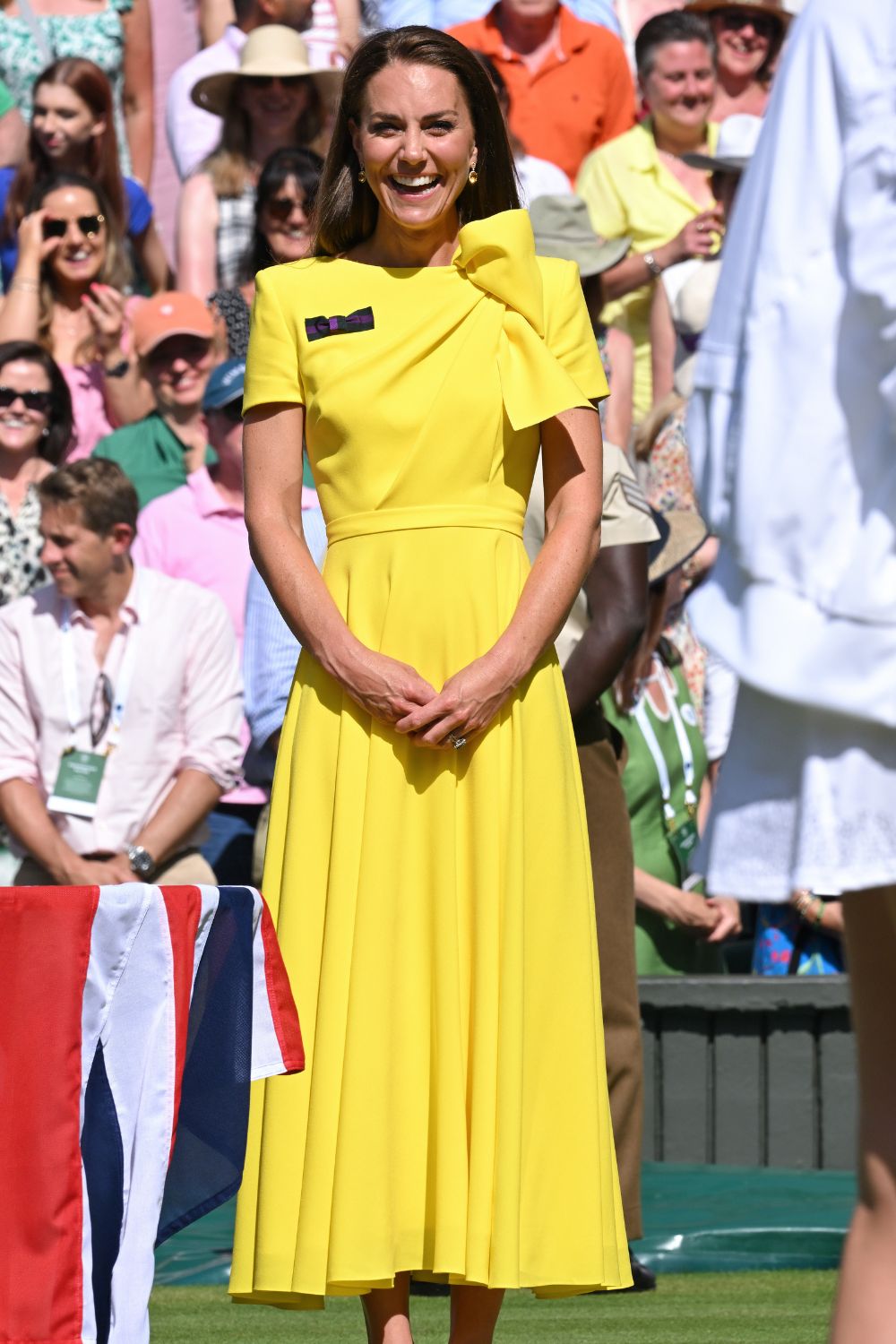 Woman in a bright yellow dress smiling at an outdoor event, surrounded by a crowd.
