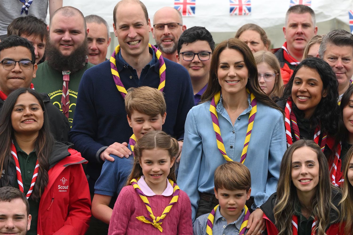 A group photo with people wearing scout scarves, including men, women, and children, smiling at the camera.