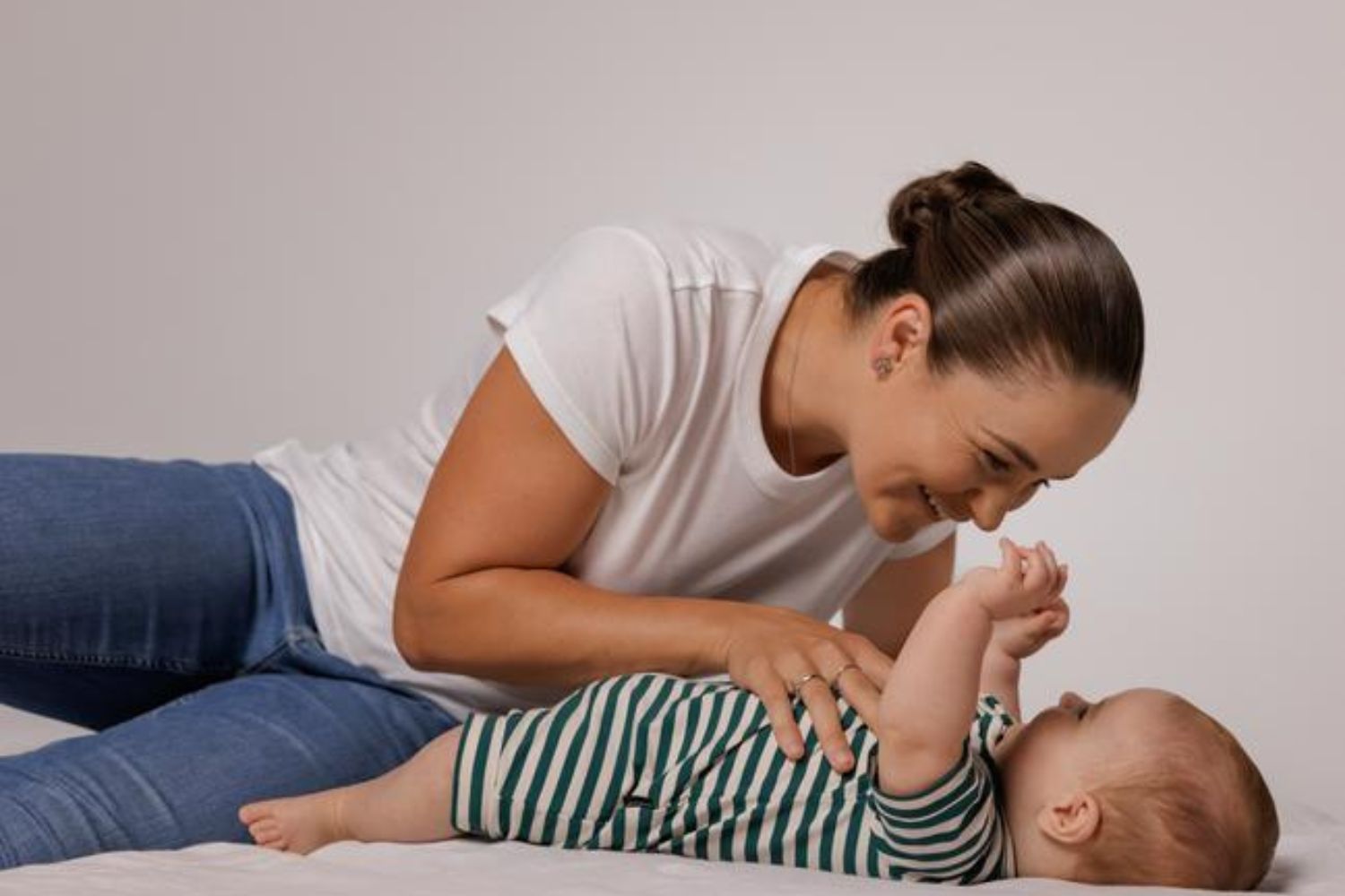 Woman smiling at baby lying down, both wearing casual outfits.