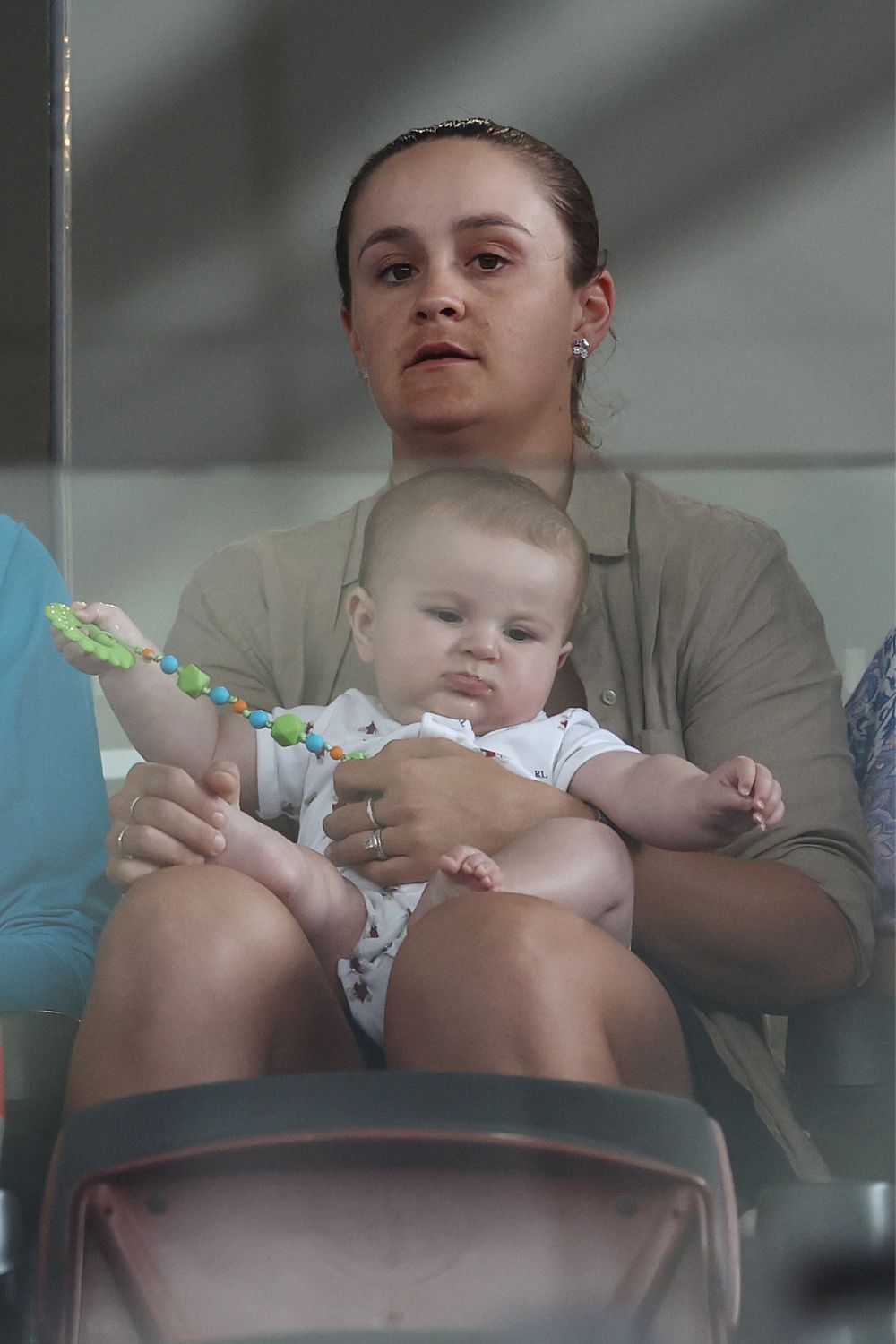 A woman holding a baby on her lap, both facing forward. The baby holds a colorful toy.