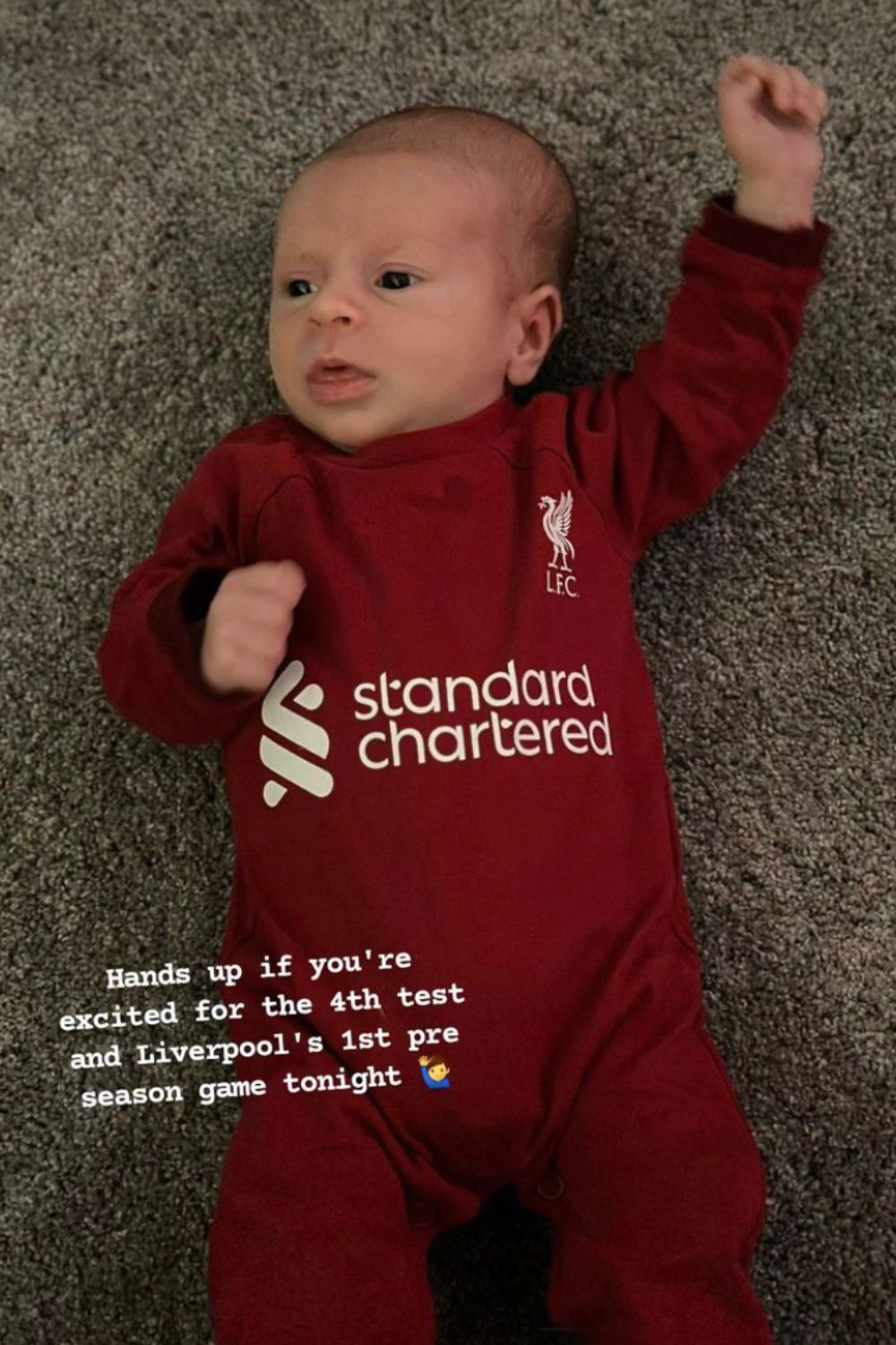 Baby wearing a Liverpool FC outfit, raising a hand on a carpeted floor, with overlay text about sports excitement.