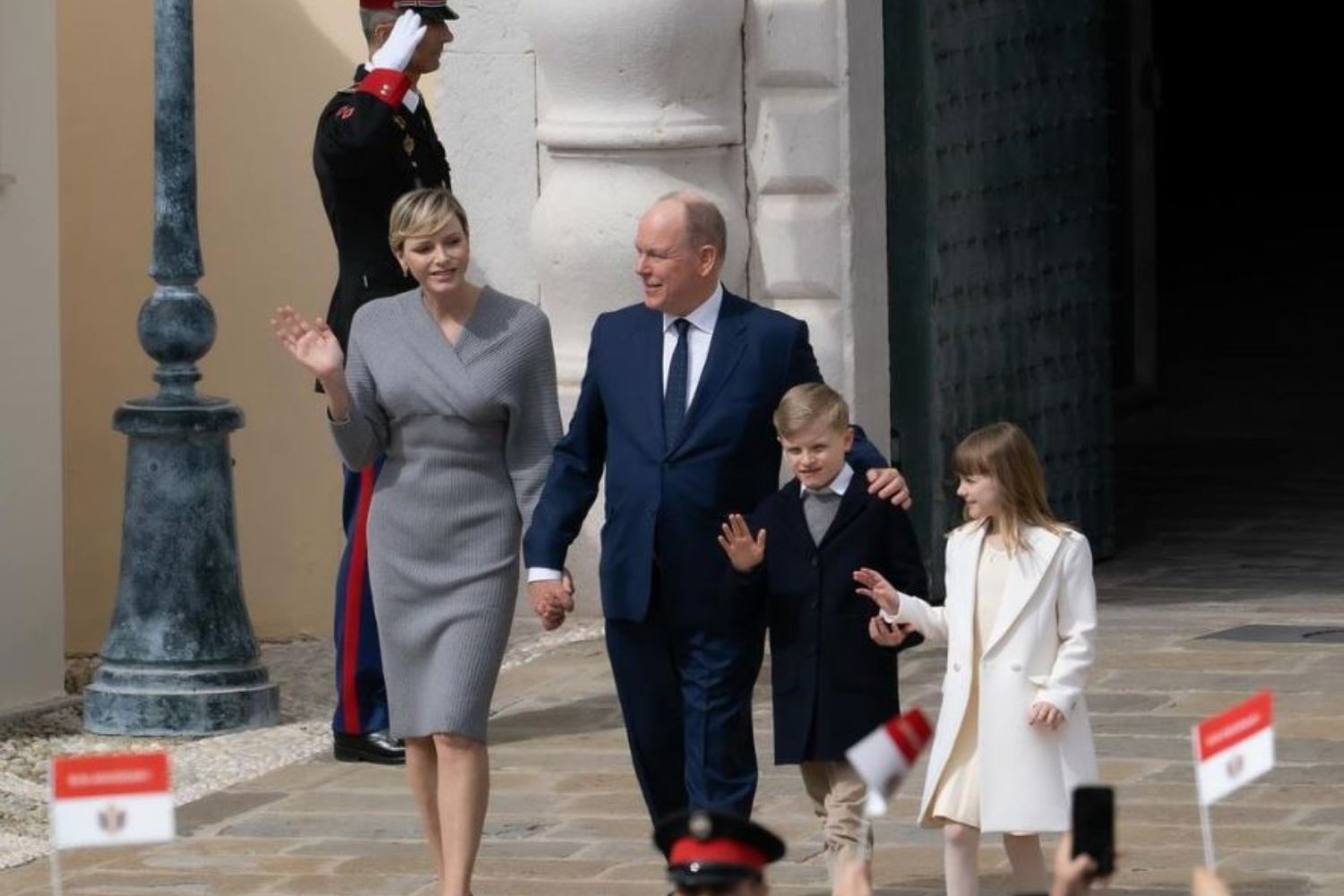 Royal family walking and waving, with a guard saluting in the background.
