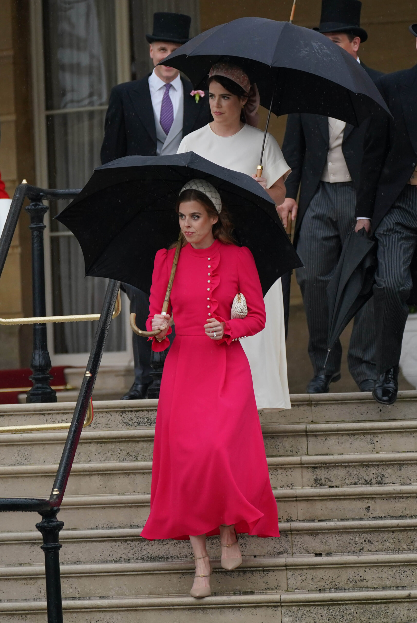 Princess Beatrice in a pink dress and headband holding an umbrella at an outdoor event.