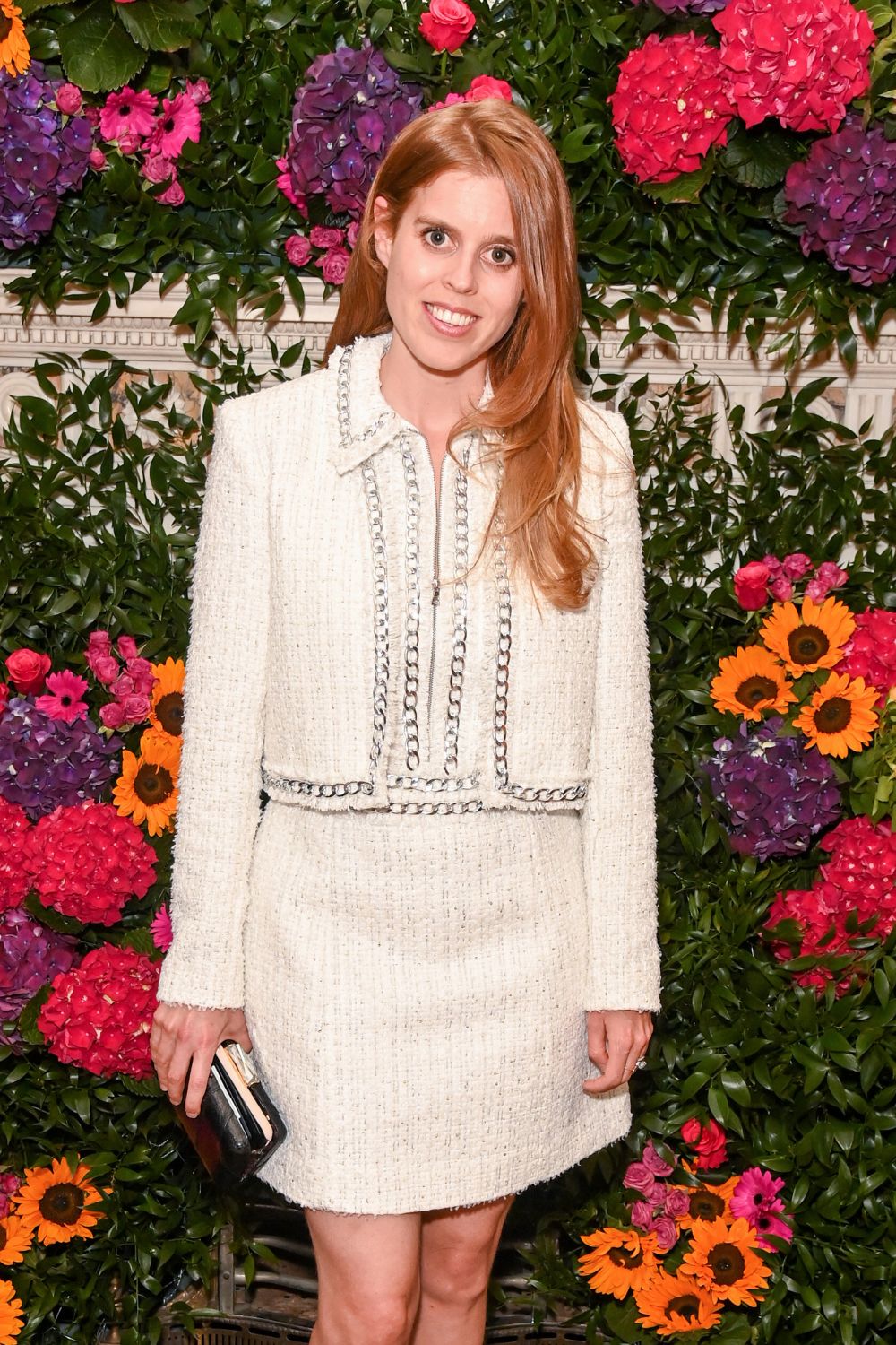 Princess Beatrice in a white suit at an event with a vibrant floral backdrop.