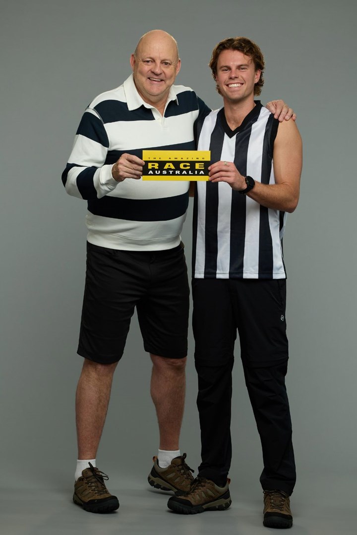 Two men wearing black and white striped shirts hold an "Amazing Race Australia" card against a gray background.