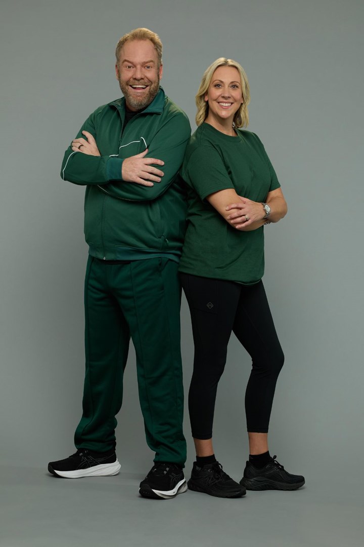 Two people in green athletic outfits stand back-to-back smiling, on a neutral gray background.