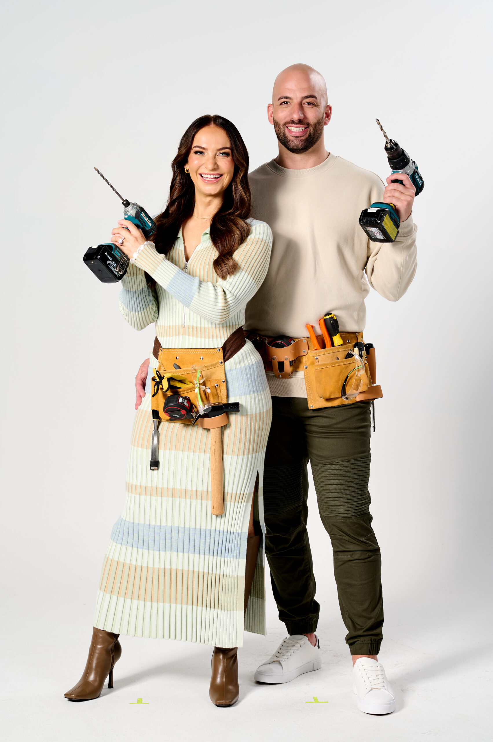 Couple in work attire holding power drills, smiling, with tool belts; "The Block" contestants 2024.