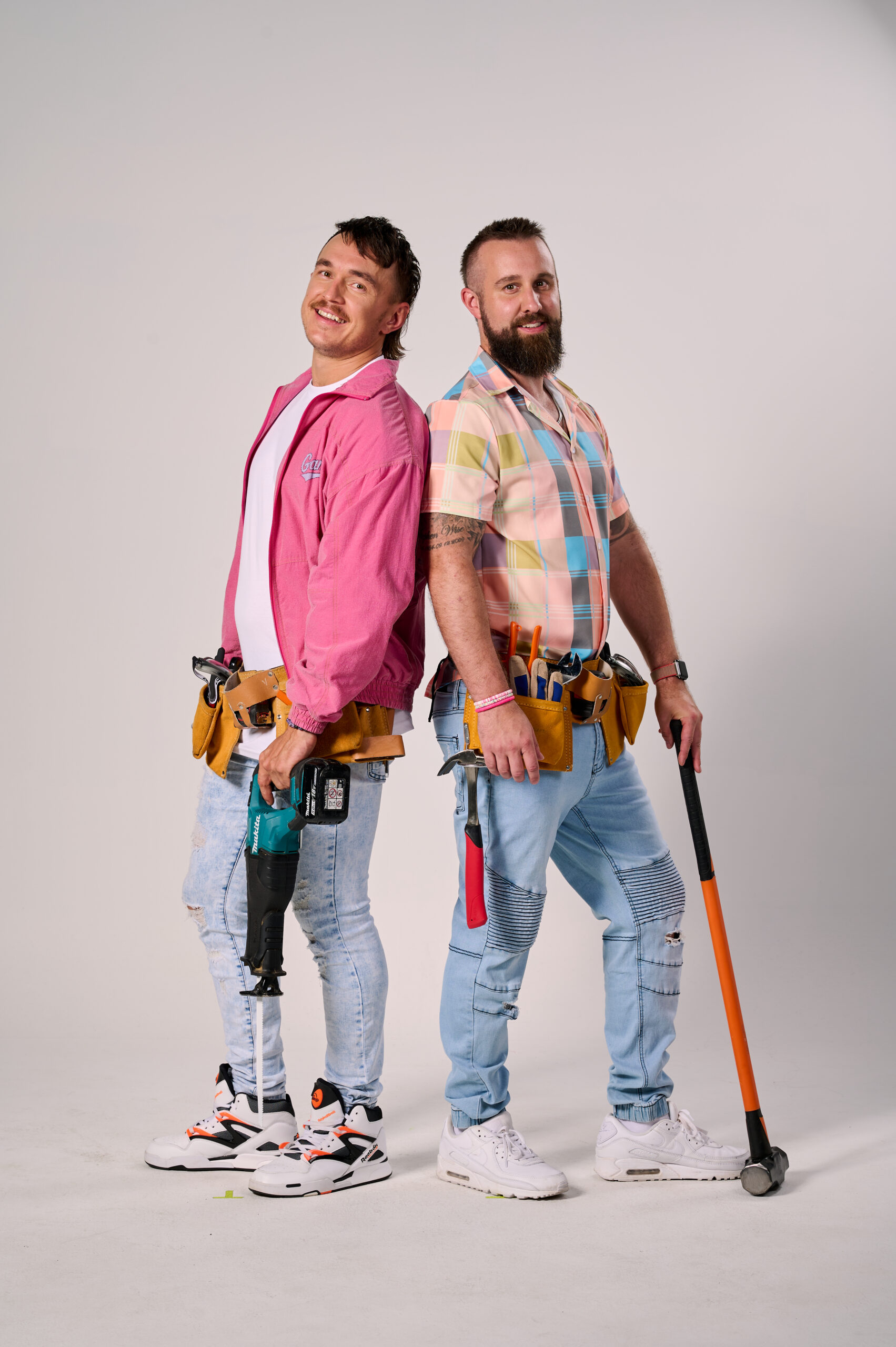 Two contestants from The Block 2024 posing back-to-back with tools and colorful outfits.