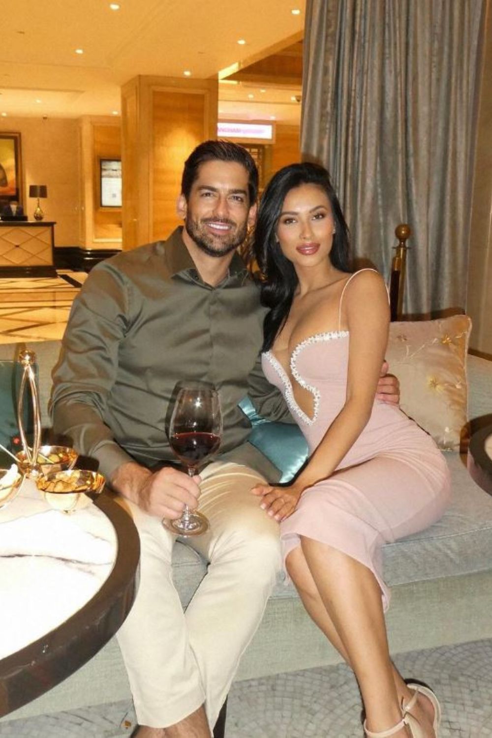 A man and woman sitting together on a sofa, with the man holding a glass of red wine.