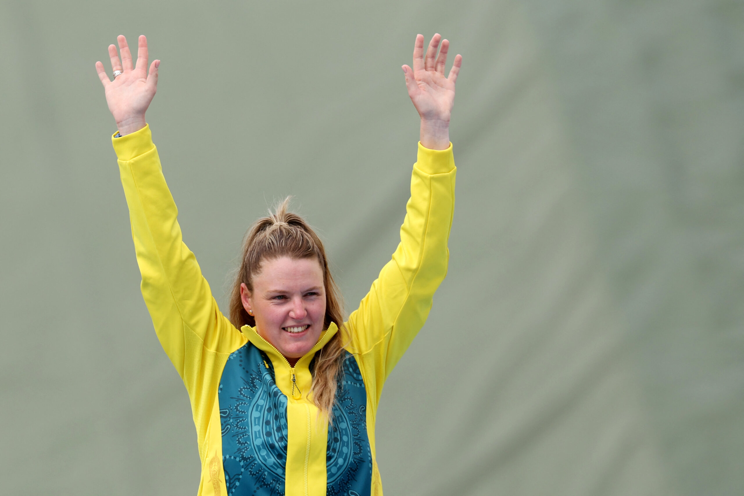 Person in yellow and green sports attire raises arms, smiling against a neutral background.