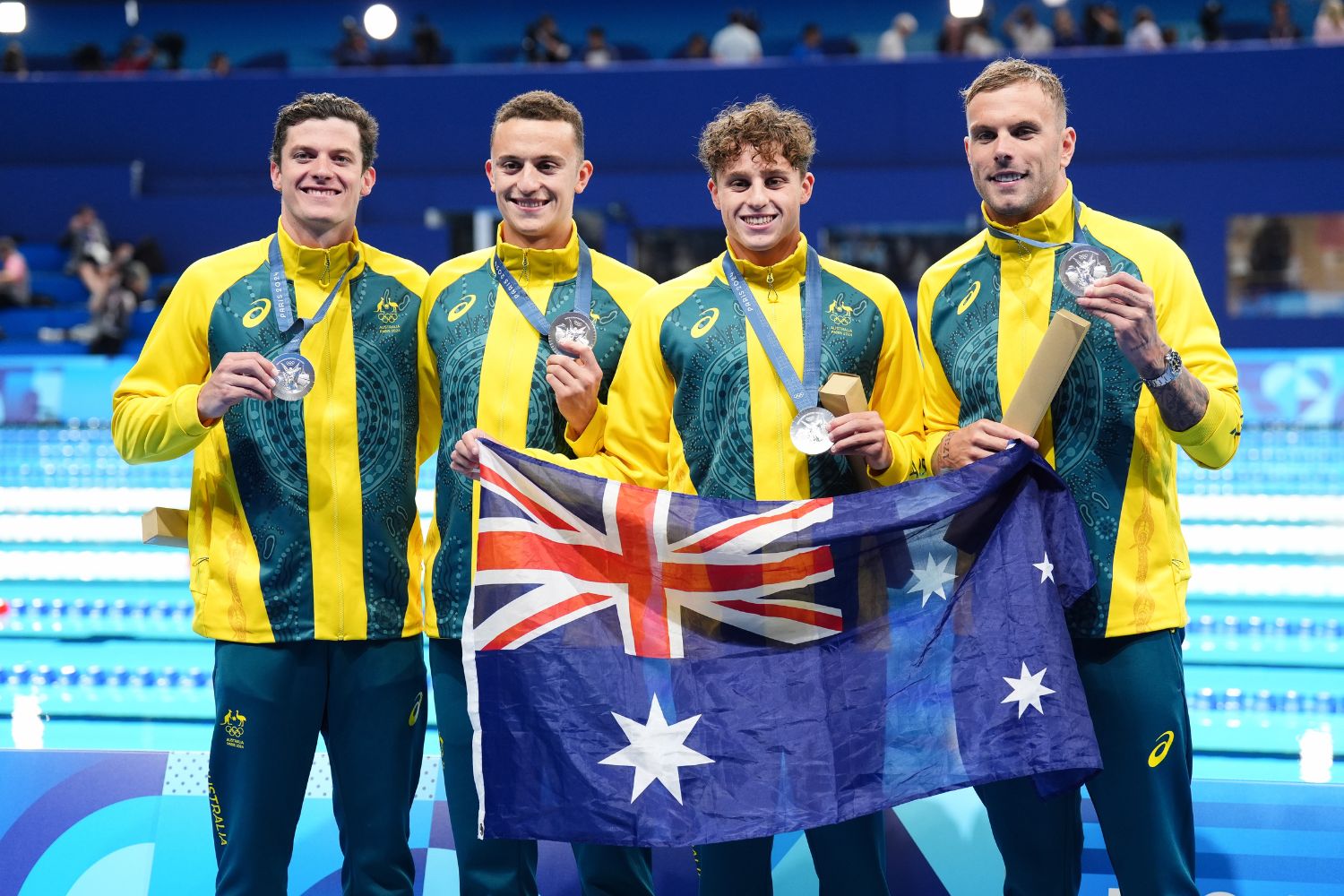 Australian men's relay swim team holding silver medals and Australian flag at World Aquatics Championships.
