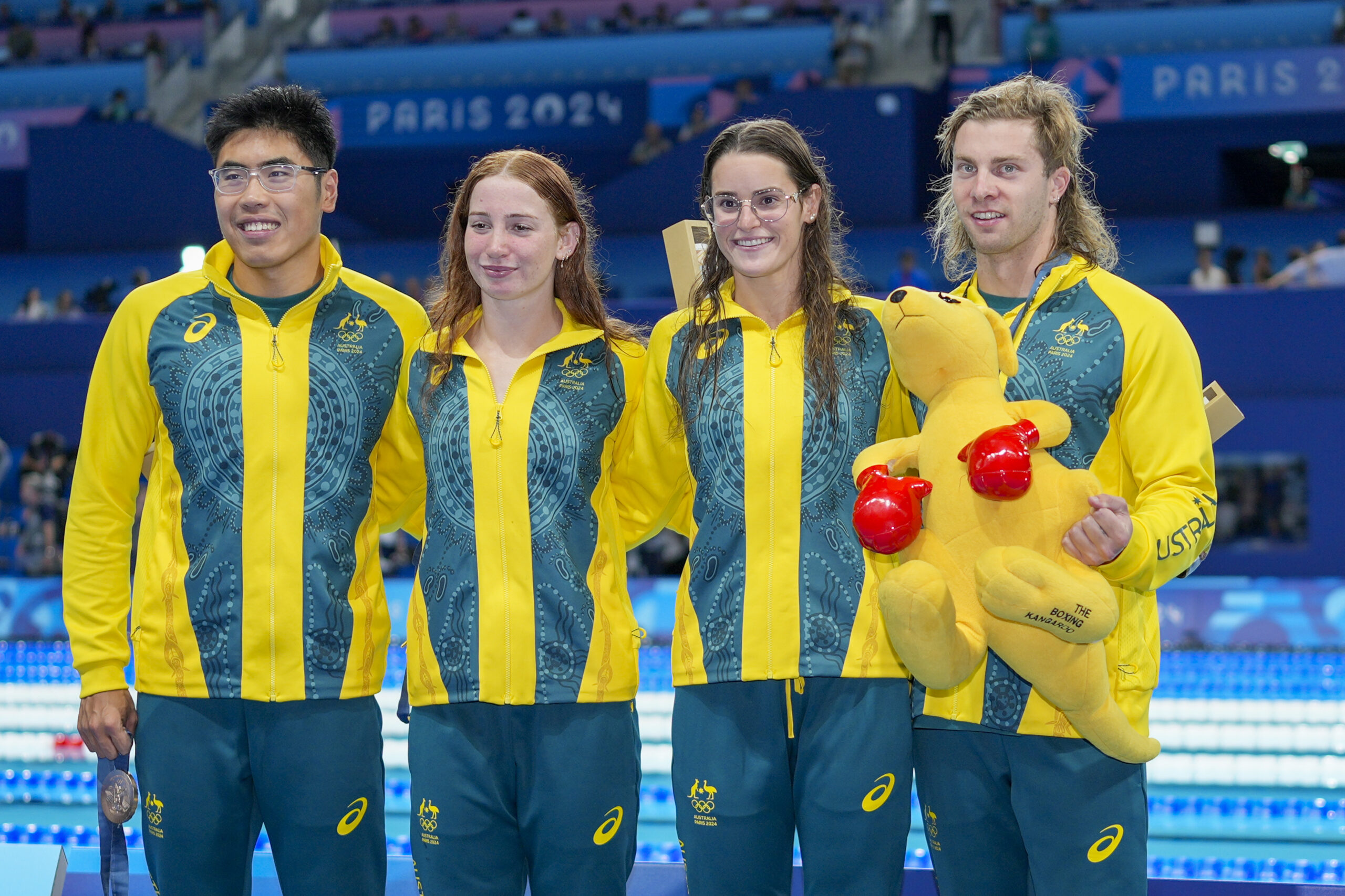 Australian swimmers in team uniforms with medals at Paris 2024, one holding a plush kangaroo.