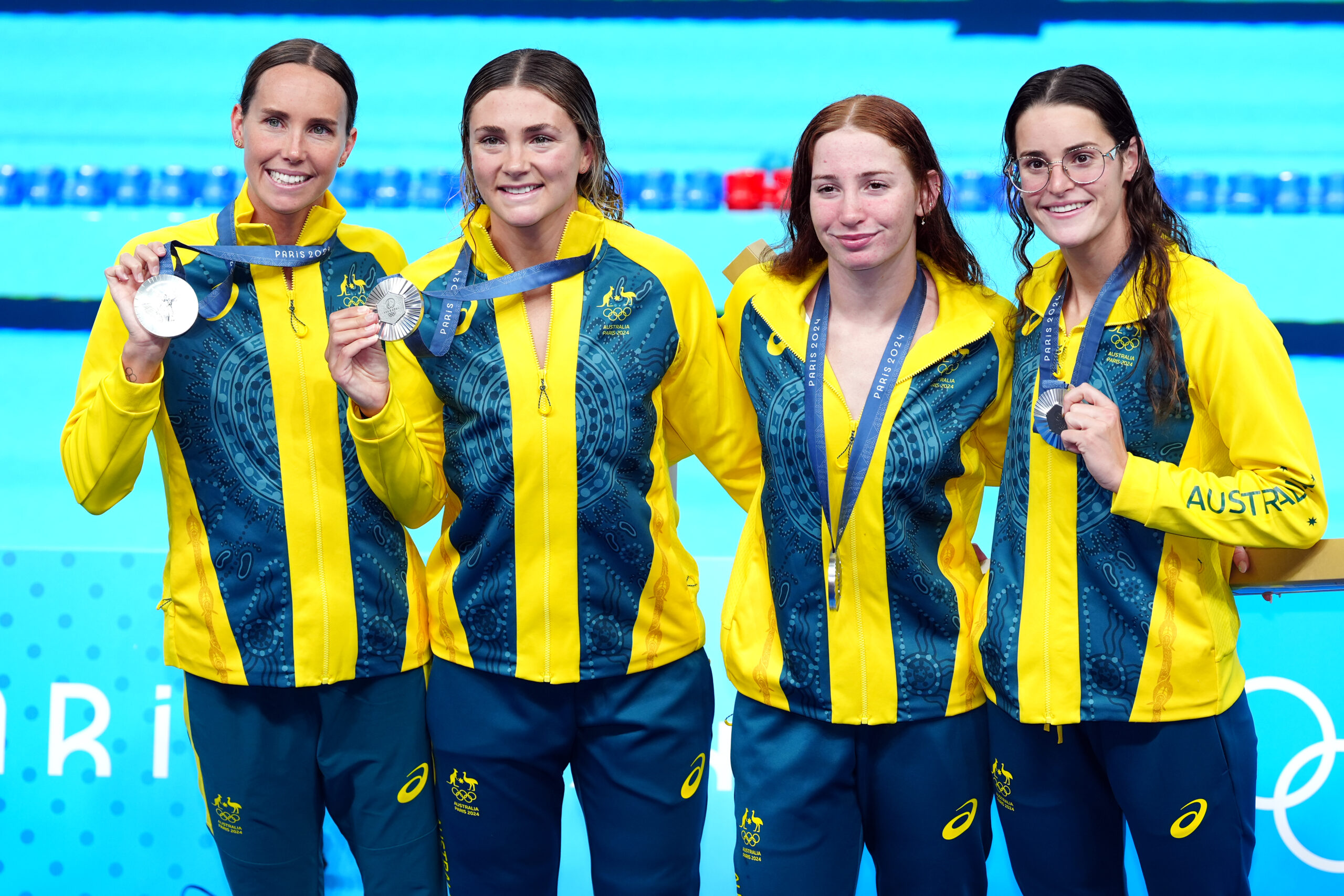Four Australian swimmers in team jackets proudly display silver medals at the Paris 2024 Olympic pool.