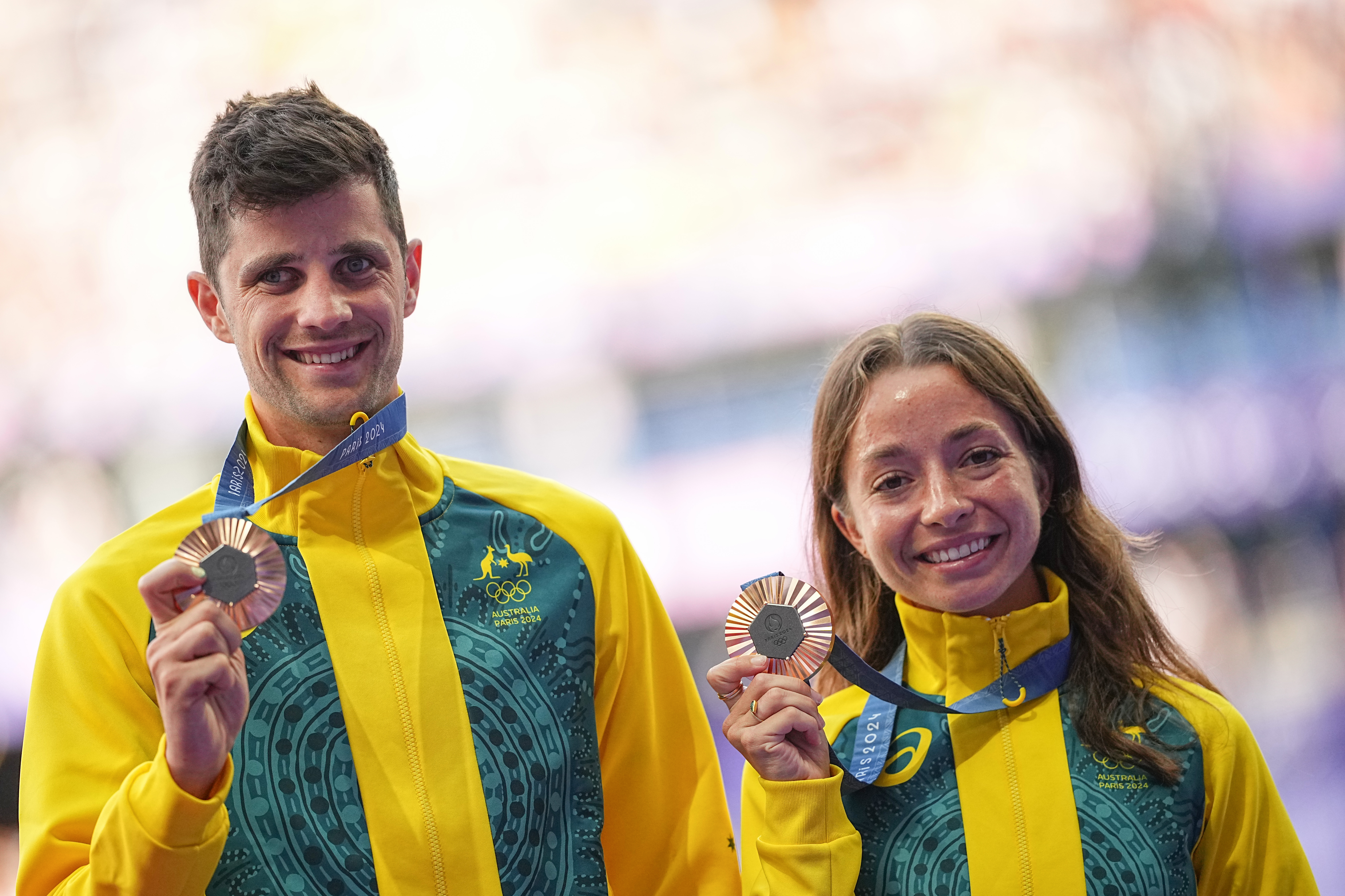Two athletes in yellow-green Australia tracksuits proudly display their medals with smiles.