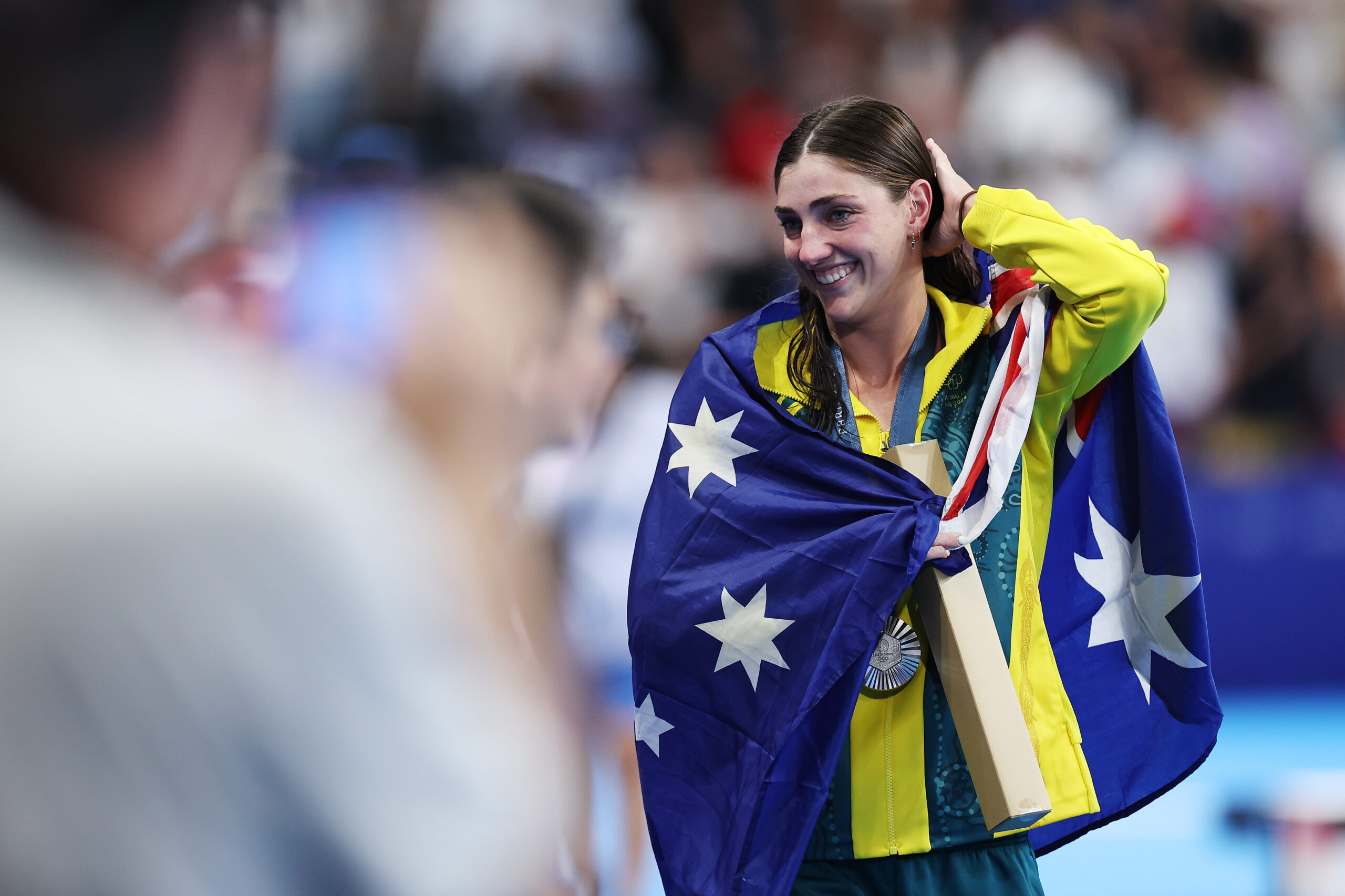 Smiling athlete draped in Australian flag, wearing a medal at a sports event.