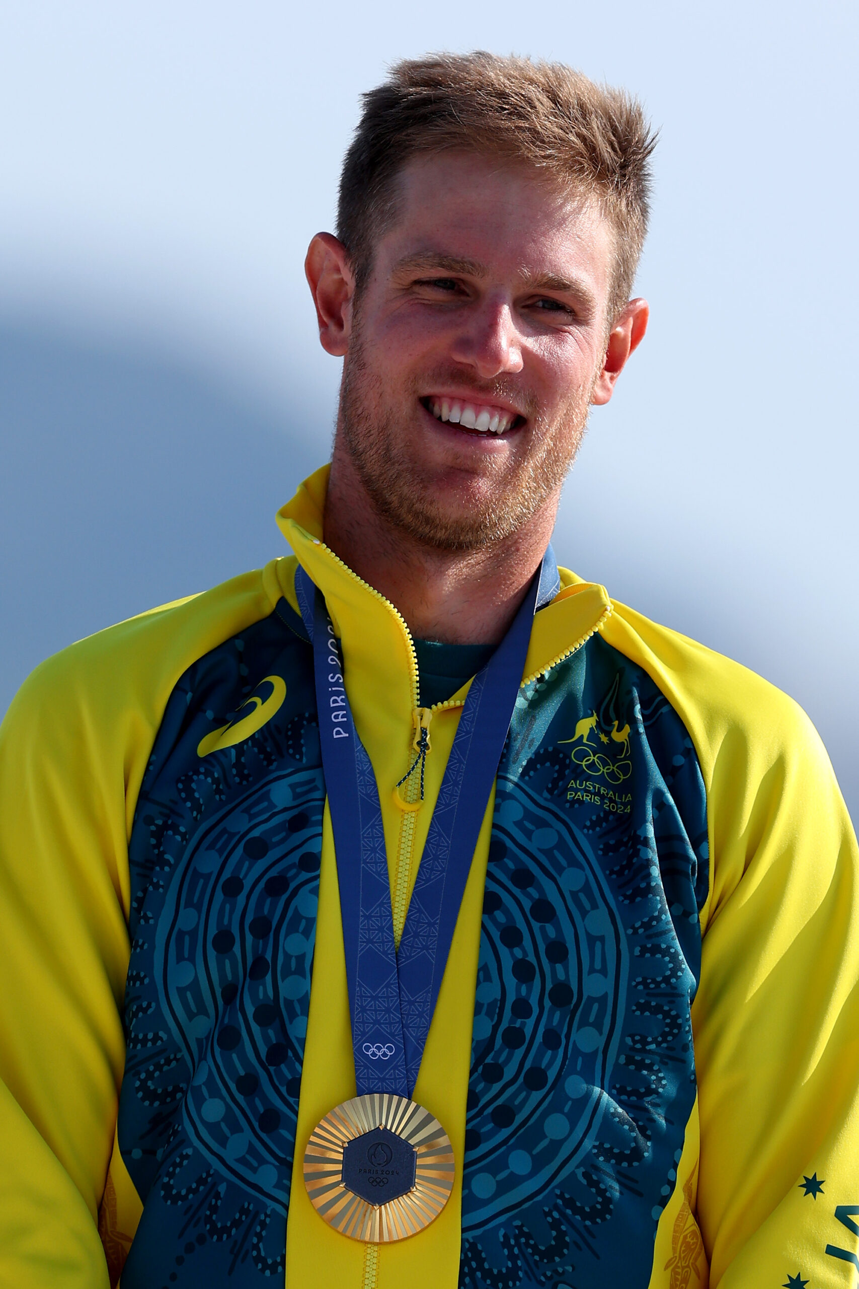 Australian athlete in yellow-green jacket with Paris 2024 medal, smiling.